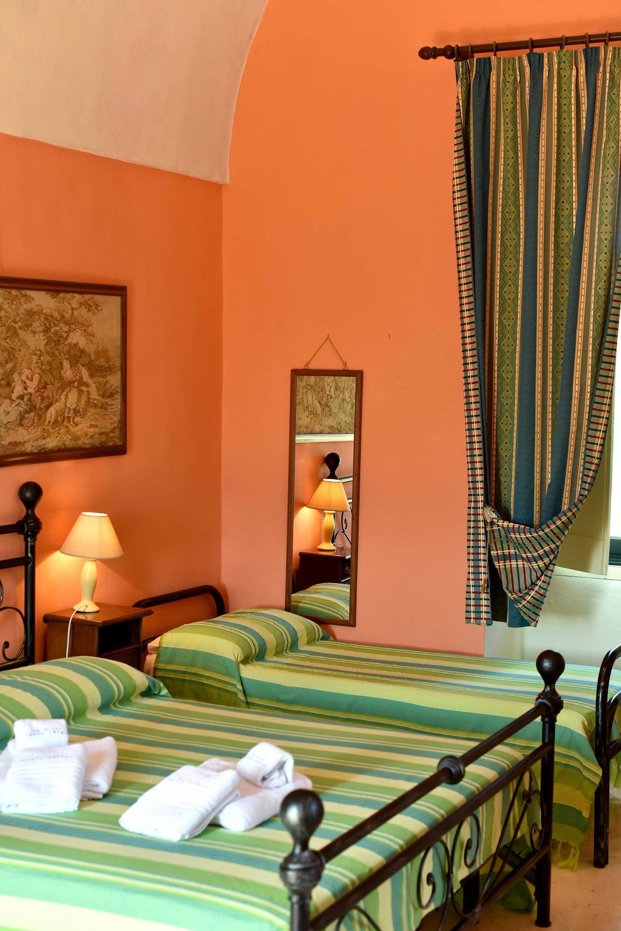 A hotel room with two beds, a mirror, a lamp, and a painting on the wall.