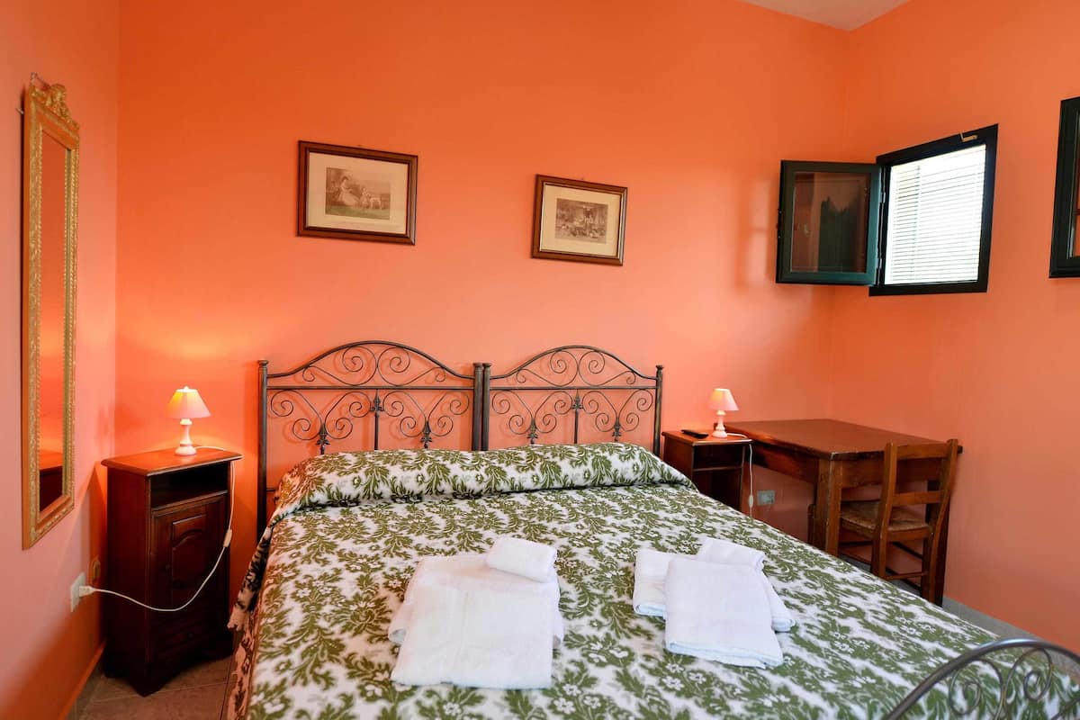 A bedroom with a bed, two bedside tables, a desk, and two framed pictures on the wall.