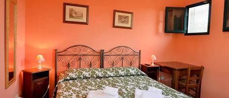 Un dormitorio con una cama, dos mesitas de noche, un escritorio y dos cuadros en la pared.