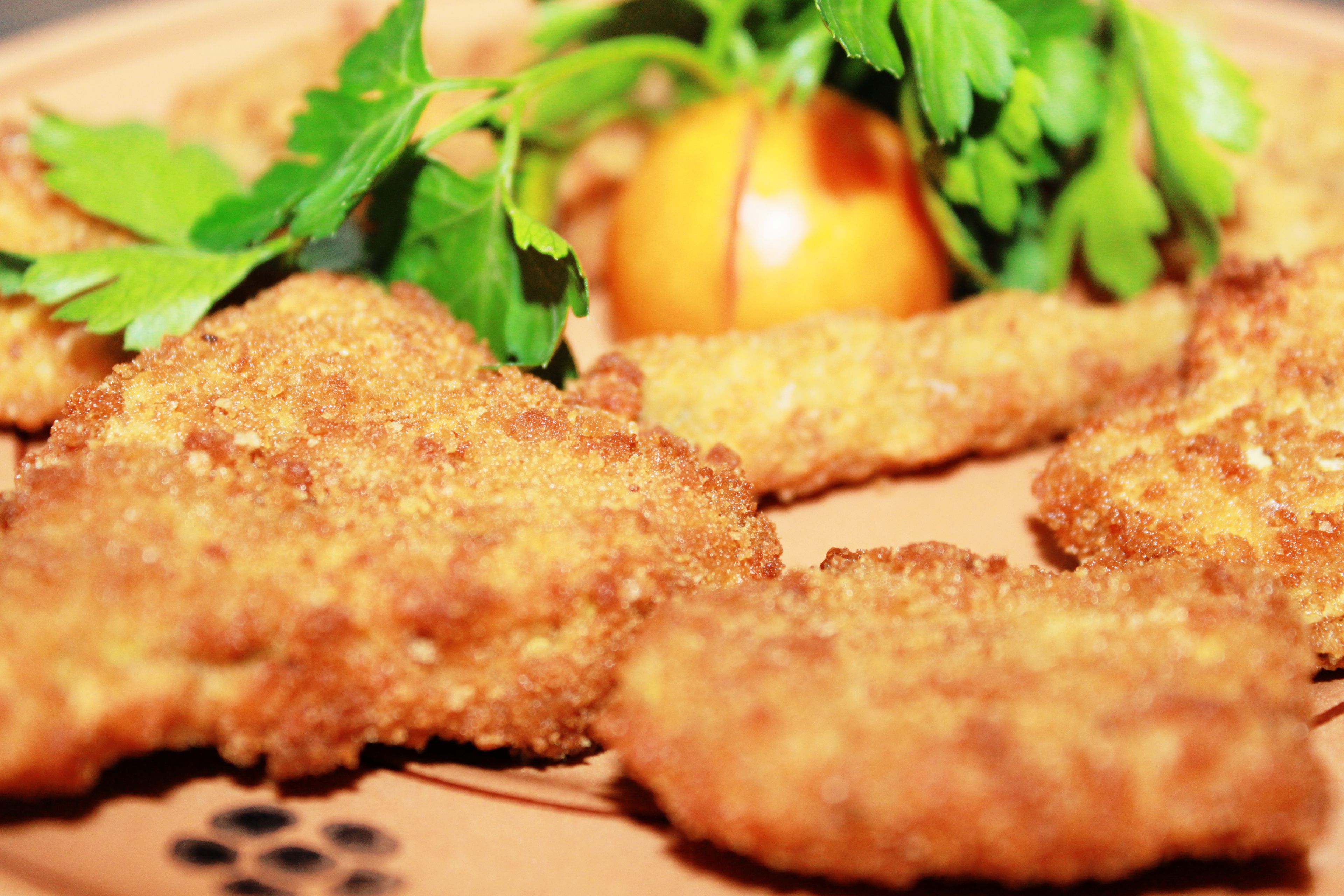 Panierte und frittierte Speisen, vermutlich Hähnchenschnitzel, auf einem Teller mit Petersilie und einer Tomate.