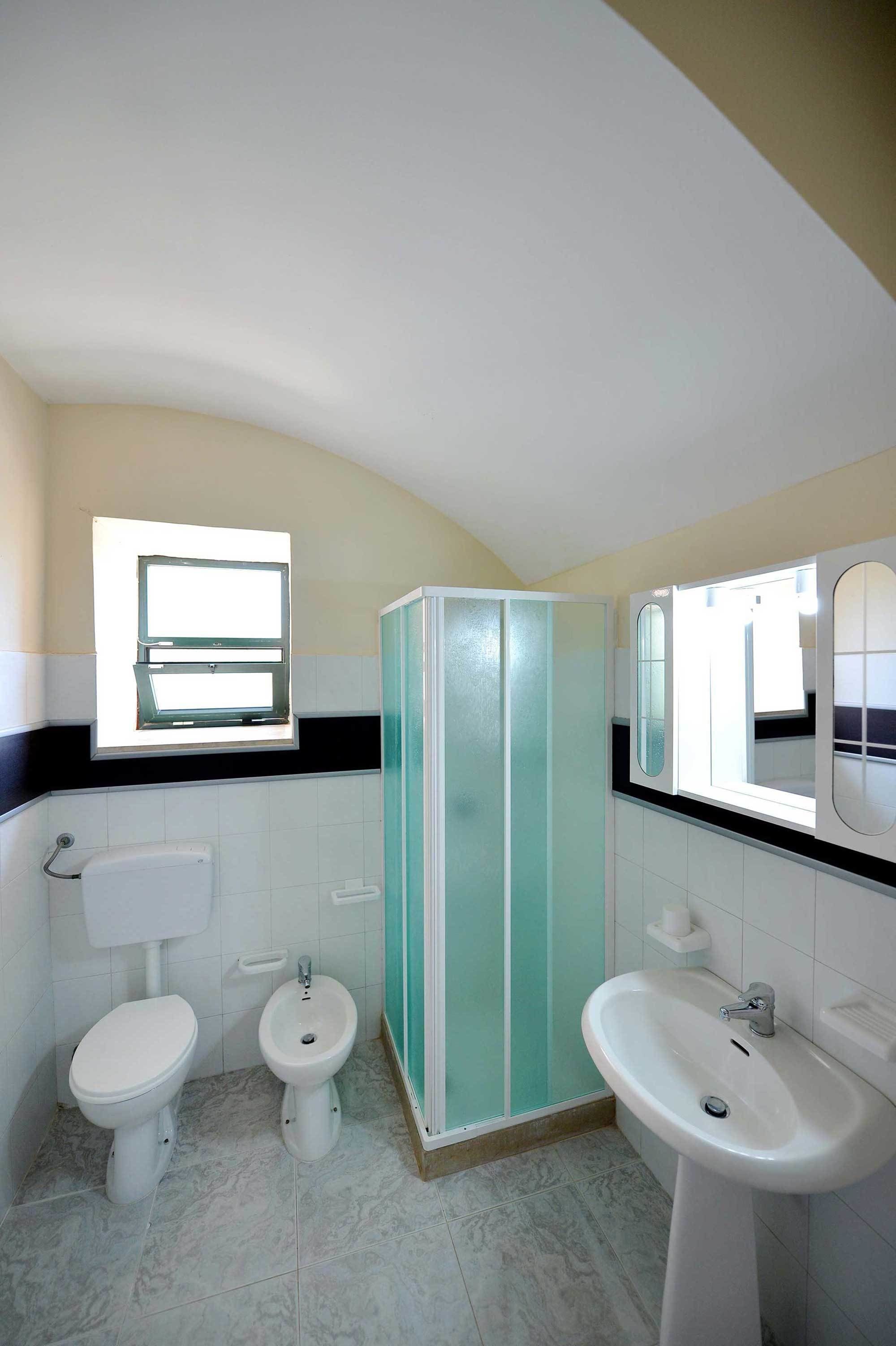 Een badkamer met toilet, bidet en wastafel, een raam en een spiegel.
