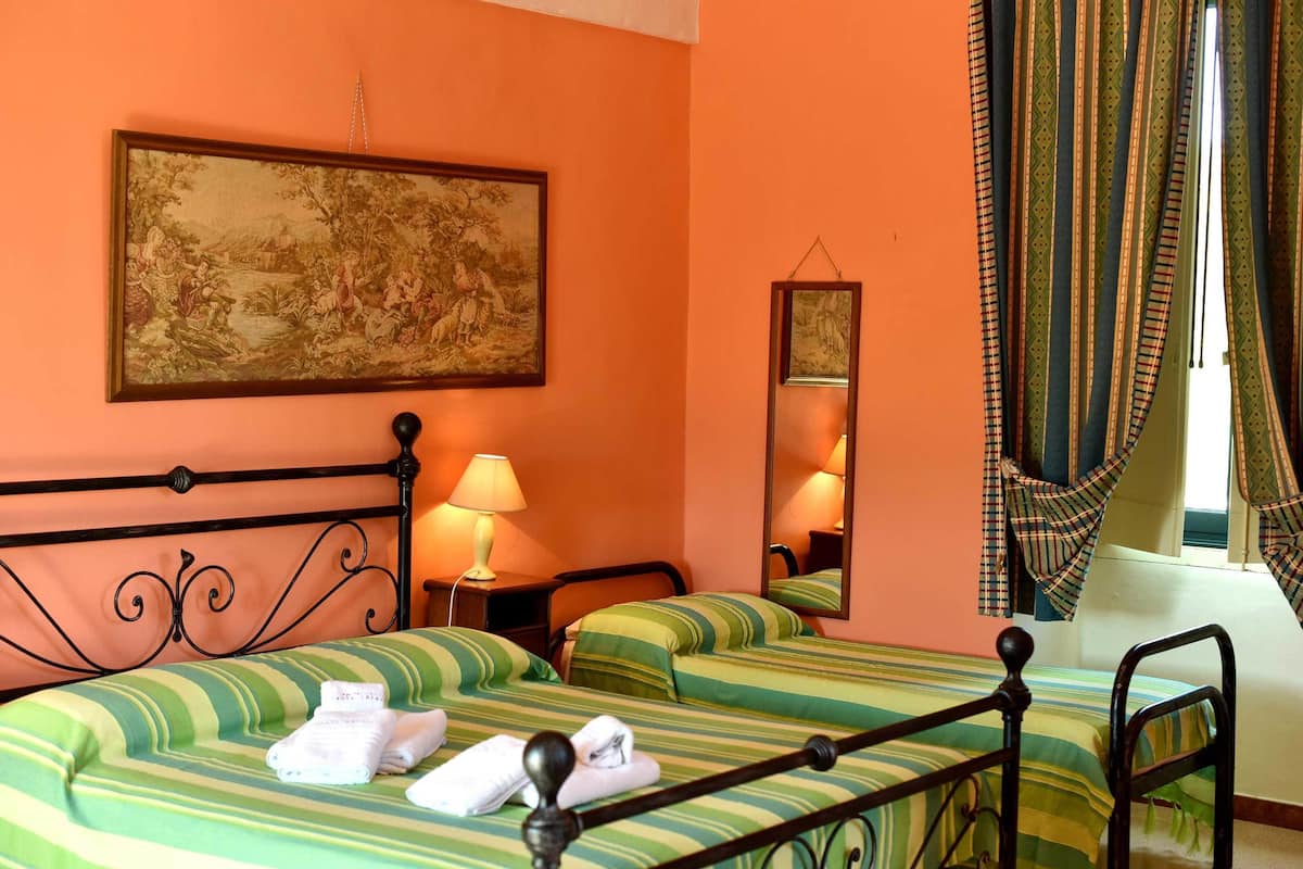 A hotel room with a bed, two pillows, a bedside table with a lamp, a mirror, and a window with curtains.