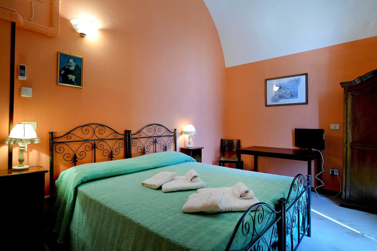 A bedroom with a bed, two bedside tables with lamps, a desk, and a chair.