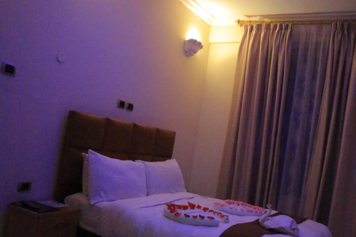 Een slaapkamer met een bed, nachtkastjes, een wandlamp en een raam met gordijnen.