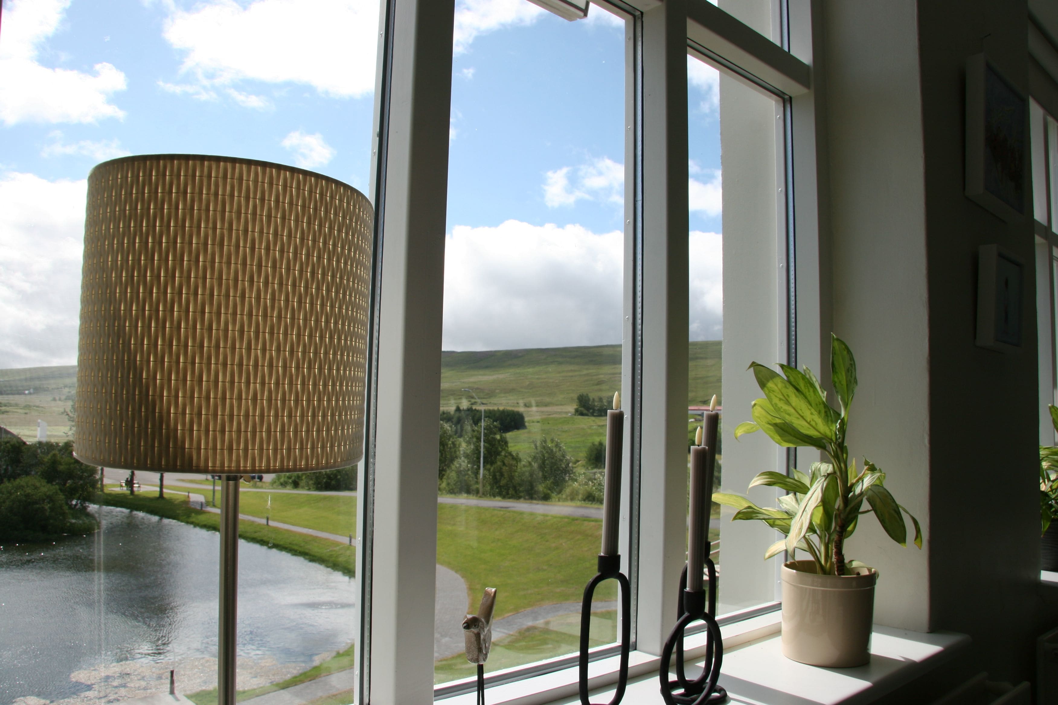 A window with a view of a landscape, a lamp, and a potted plant.
