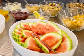 Un bufé de desayuno con diversos alimentos, incluyendo sandía en rodajas, cereales y otros productos para el desayuno.