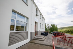 Een hotelgevel in het wit, met een naambord en een parkeerplaats met een rode reling.