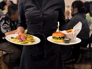 A waiter holding two plates of food, one with a burger and the other with a dish containing asparagus and other vegetables. - Hotel Laugar (Laugar)