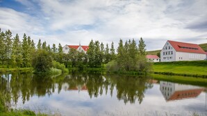 A serene lakeside setting with a white building featuring a red roof, surrounded by lush greenery and trees. - Hotel Laugar (Laugar)