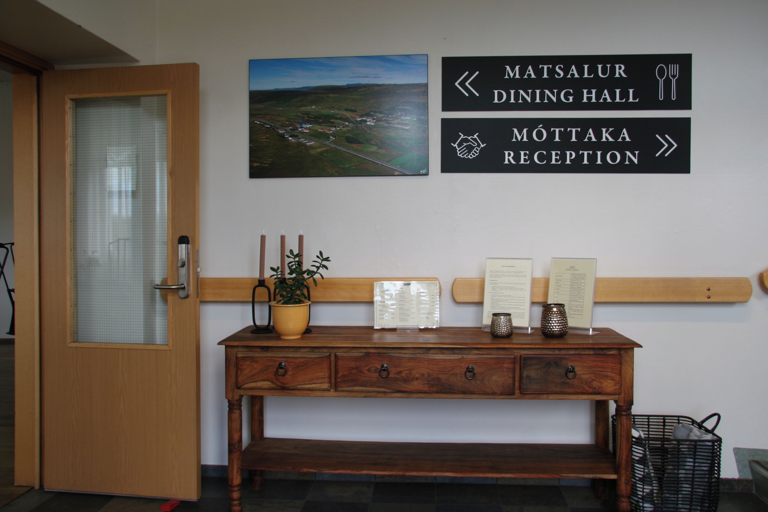 A reception desk with a wooden bench, a potted plant, and directional signs for dining hall and reception.