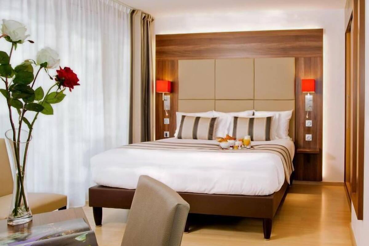 Habitación de hotel con cama, lámparas de noche, un jarrón con flores y un escritorio con una computadora port átil.