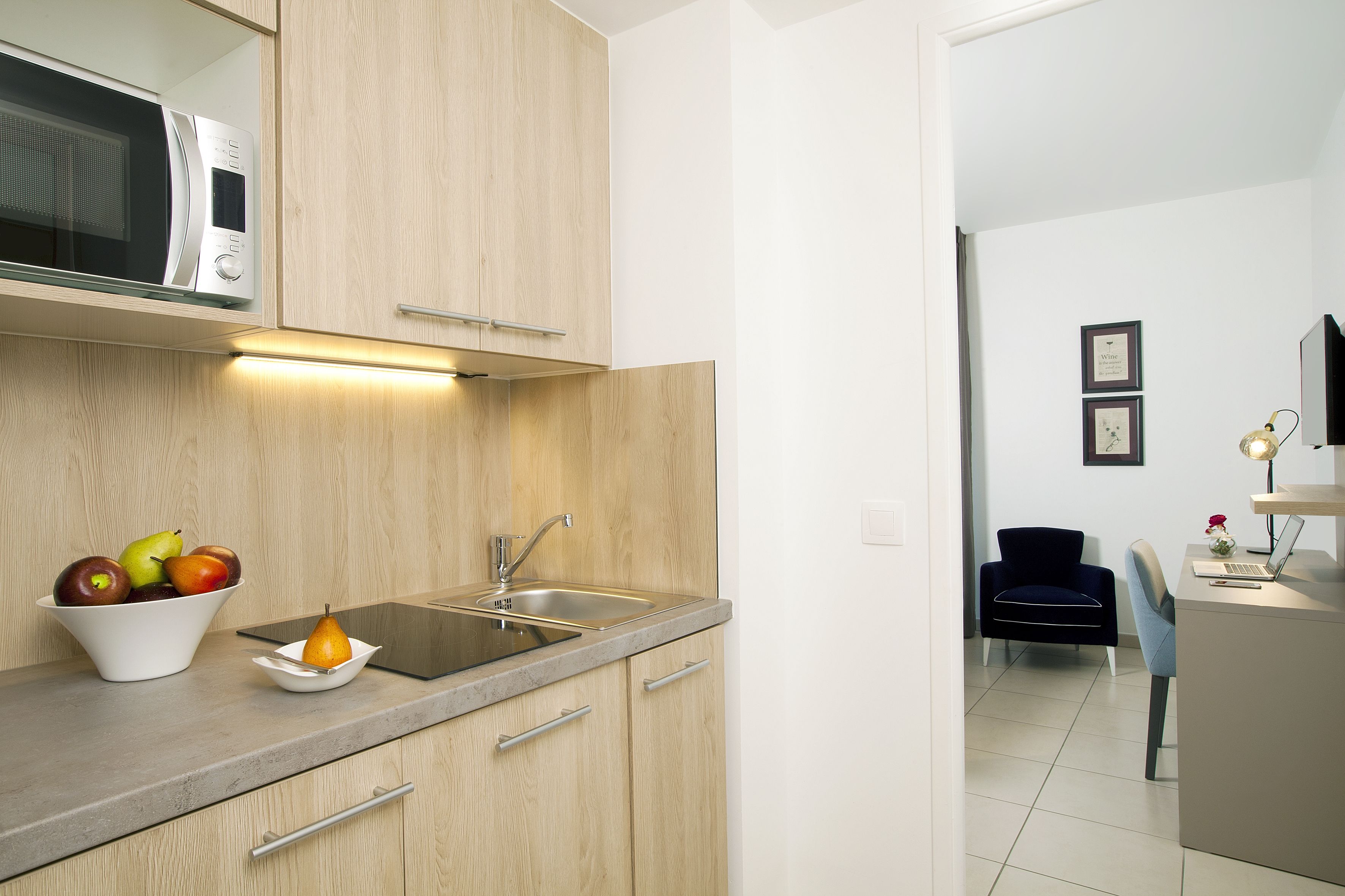 Cocina moderna con armarios de madera, microondas integrado, un lavamanos y un bol con fruta.