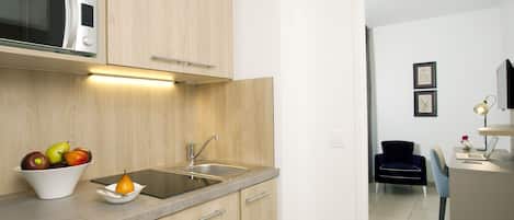Cocina moderna con armarios de madera, microondas integrado, un lavamanos y un bol con fruta.