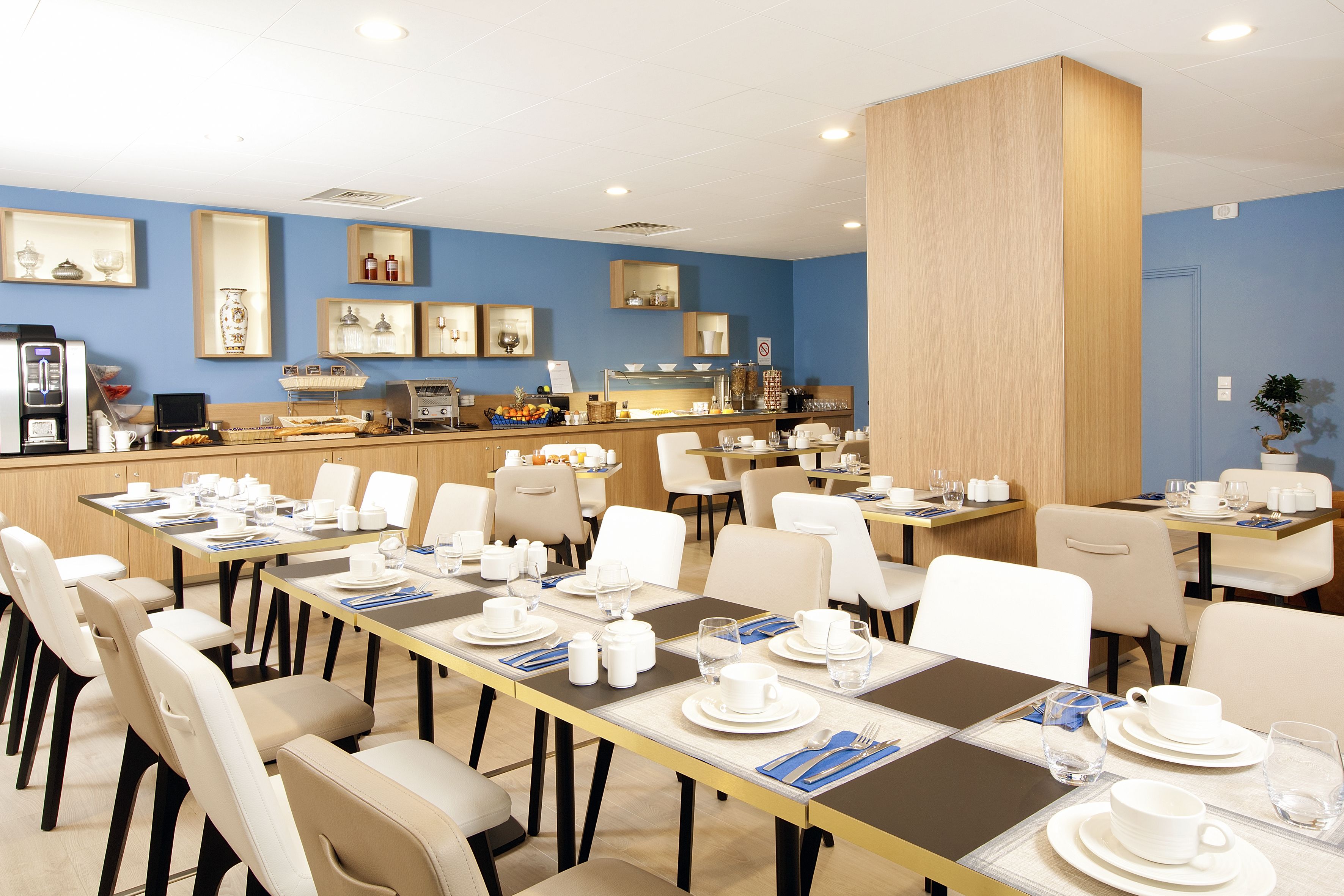 Een restaurantgedeelte in een hotel, met meerdere tafels gedekt voor het ontbijt, voorzien van witte serviesgoed en stoelen.