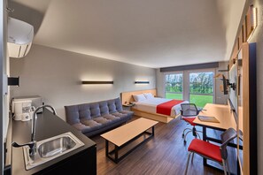 Habitación de hotel moderna con kitchenette, sofá, cama, escritorio y vistas al exterior.