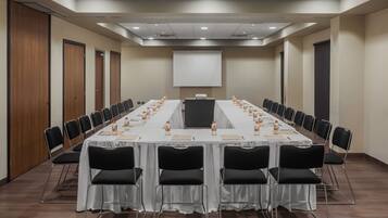 Un salón de conferencias con una larga mesa, sillas negras y una pantalla de proyector.