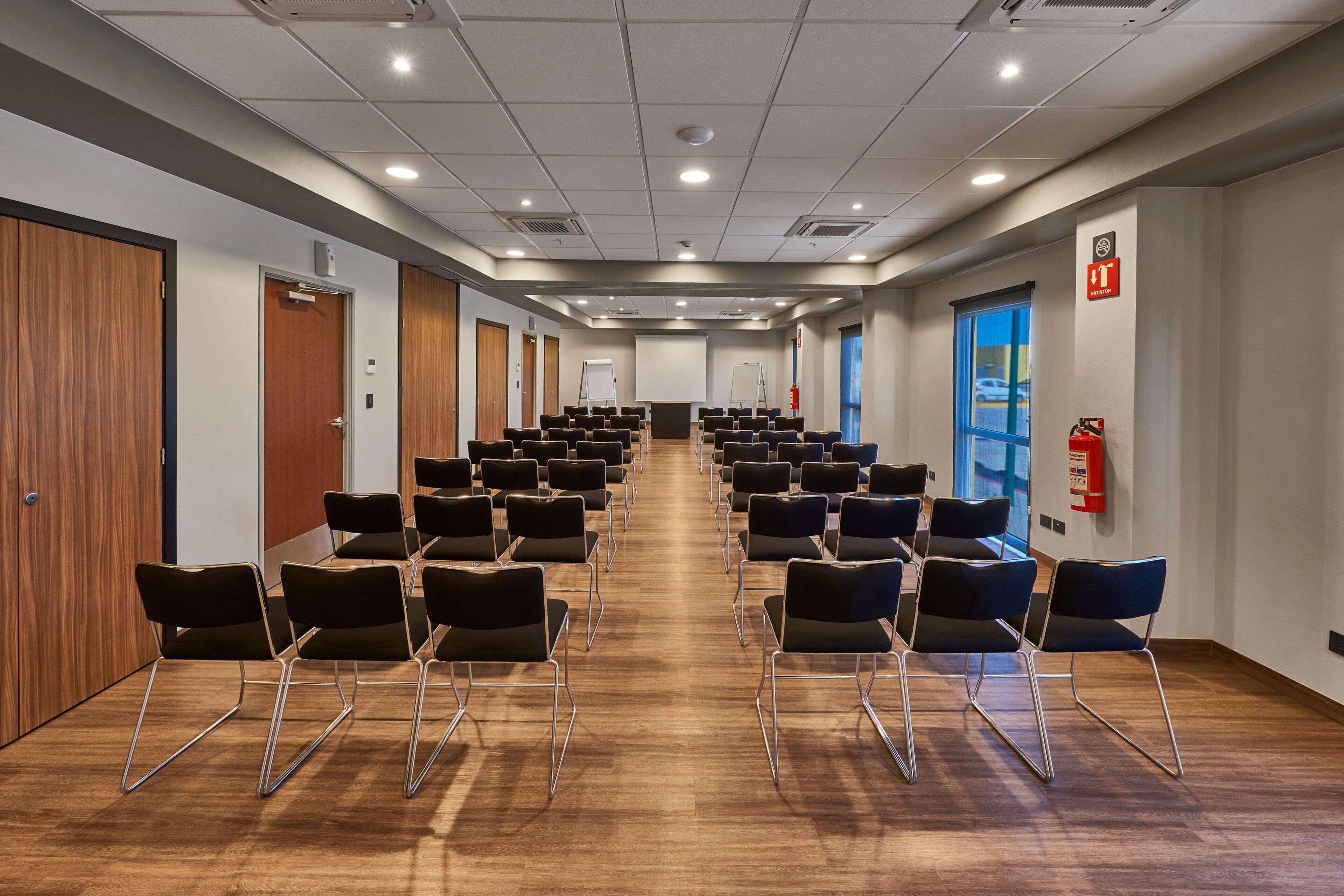 Un salón de conferencias con filas de sillas, una pizarra y un extintor.