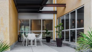 An outdoor seating area with a table and chairs, potted plants, and a building with large windows. - City Express by Marriott Celaya Galerias (Celaya)