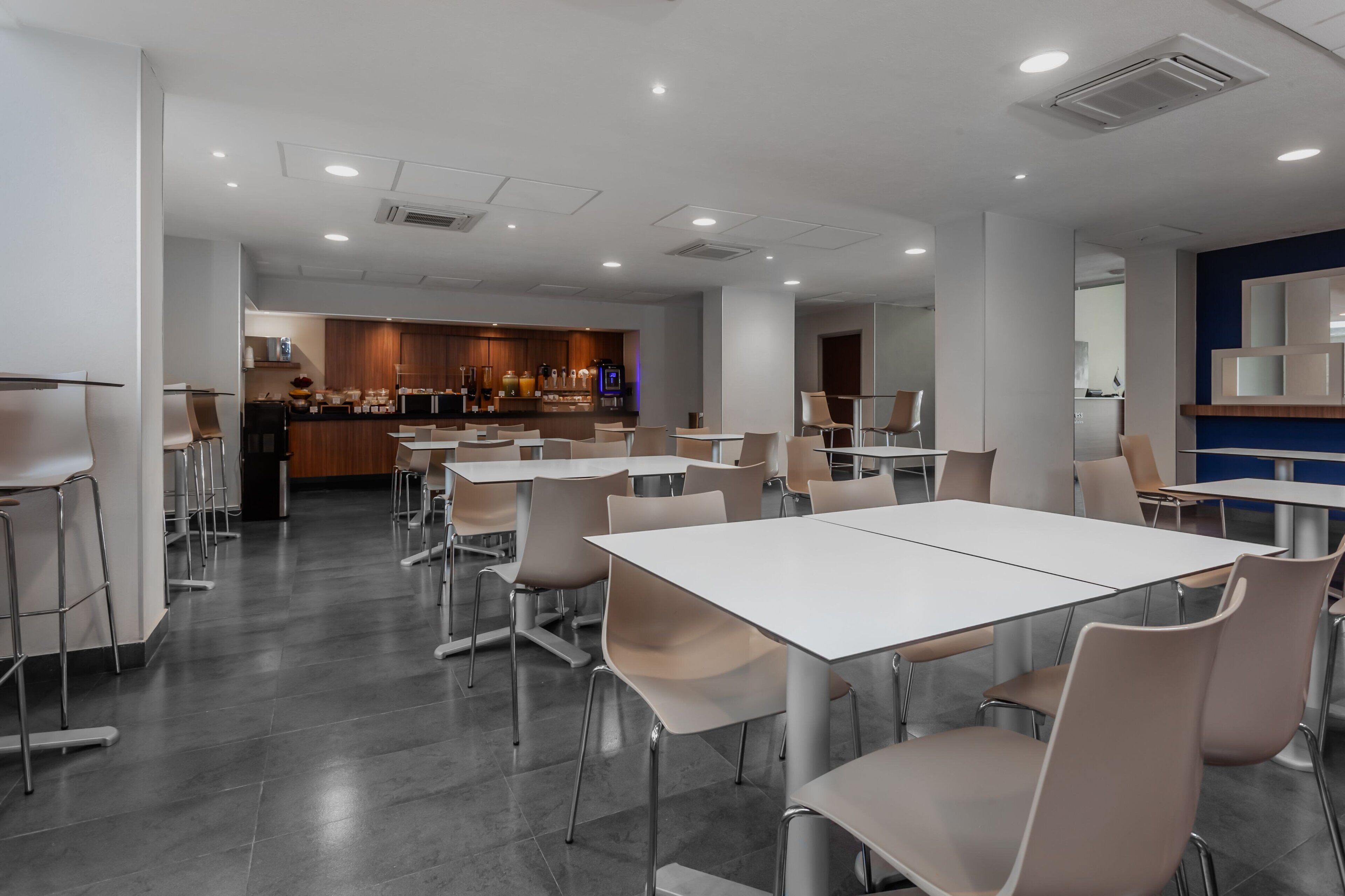 Un espace de repas moderne avec des tables et des chaises blanches, une cuisine en arrière-plan et un mur d’accent bleu.