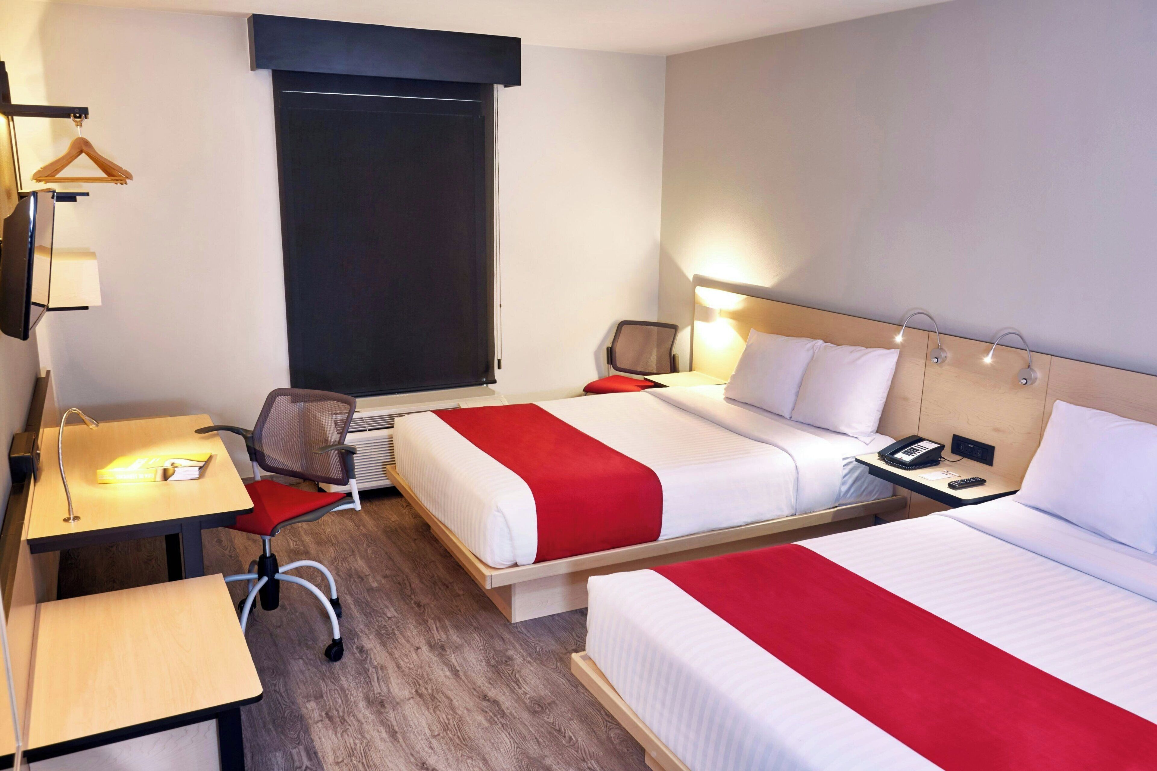 A hotel room with two beds, a desk, a chair, a TV, and a window.