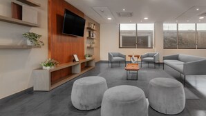 A modern waiting area with grey sofas, ottomans, and a flat-screen TV mounted on the wall. - City Express by Marriott Celaya Galerias (Celaya)