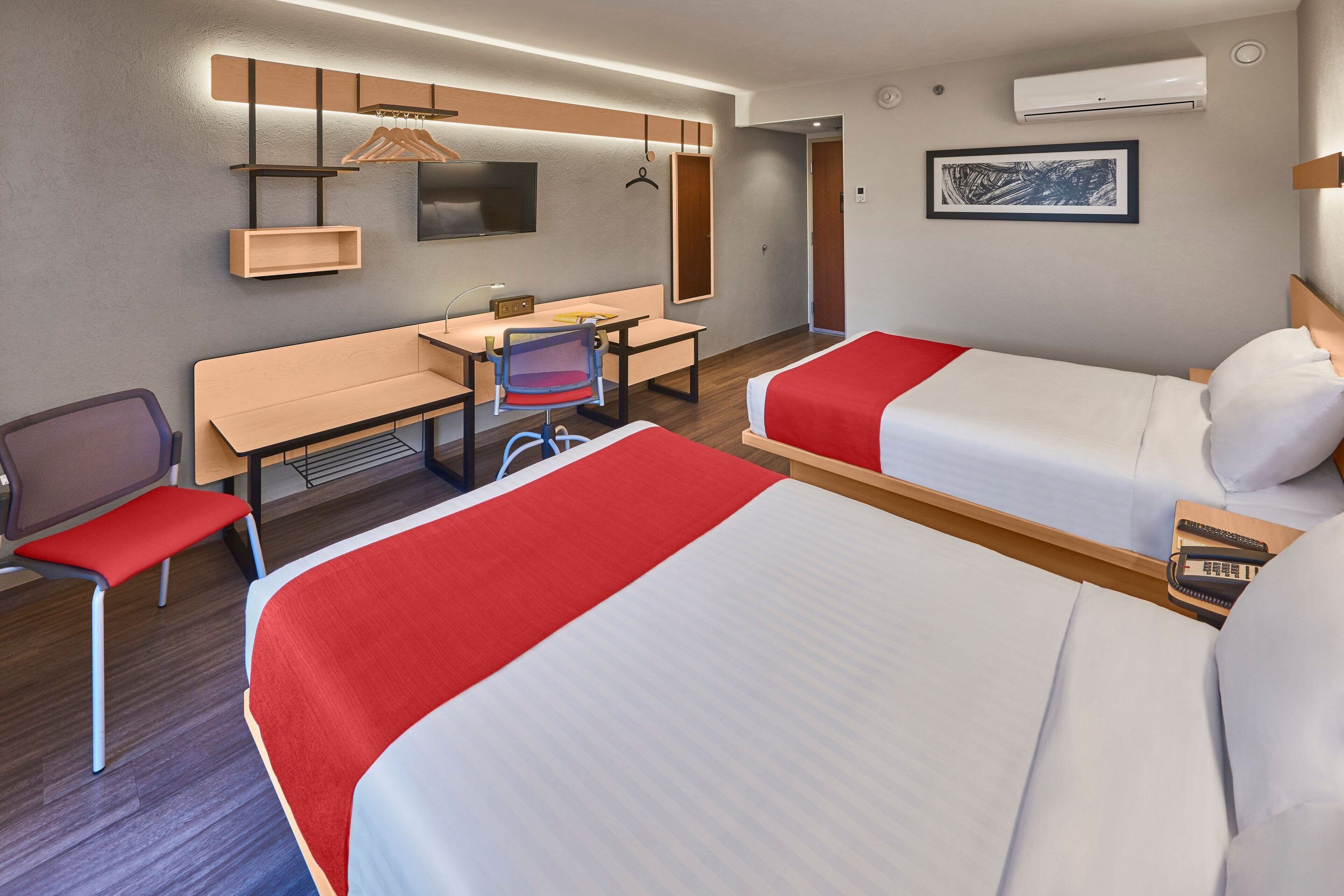 Habitación de hotel con dos camas, un escritorio, una silla, un televisor y aire acondicionado.