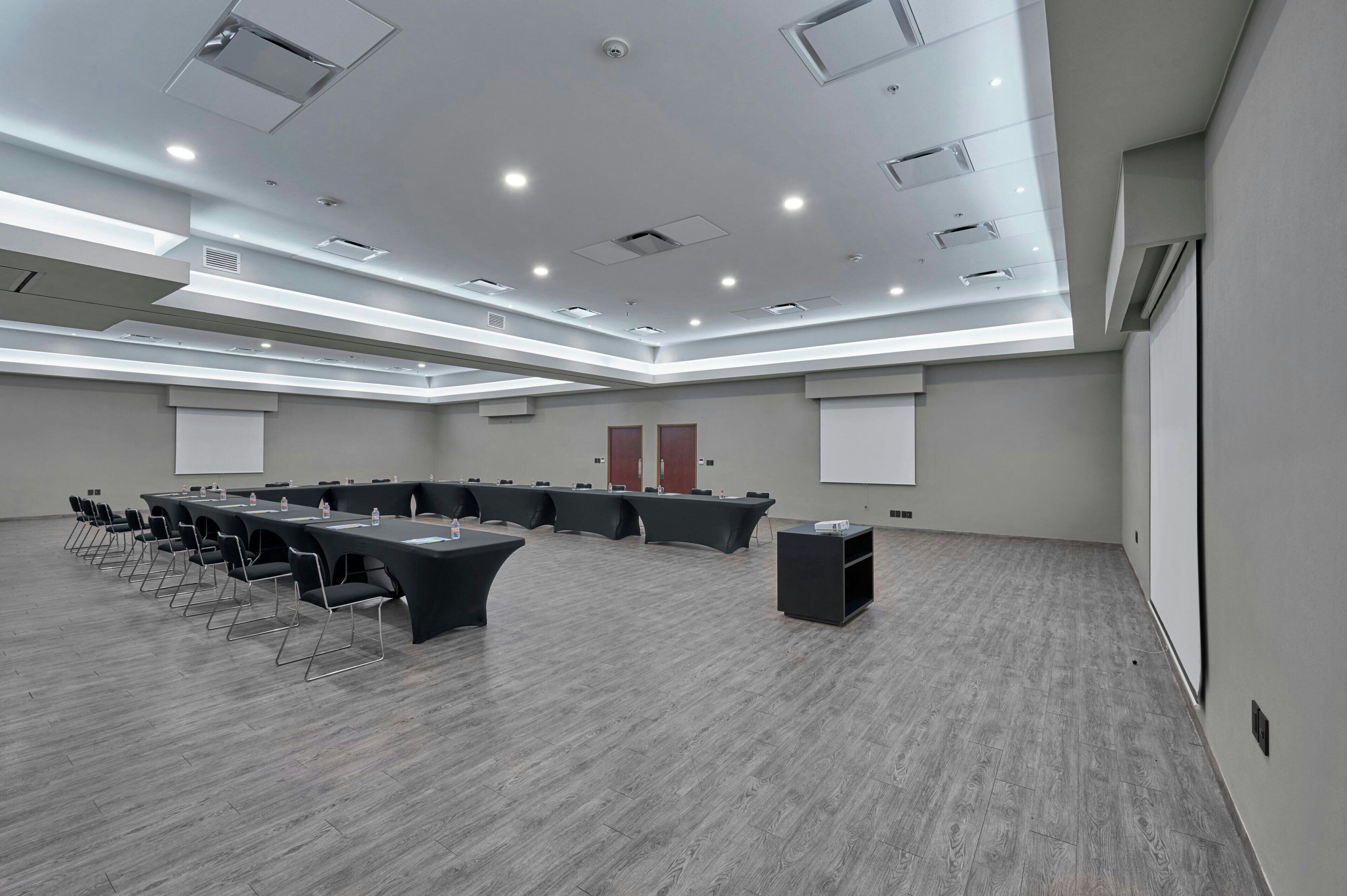 Un salón de conferencias con una larga mesa, sillas, una pantalla de proyector y una pizarra.