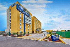 Un Hotel CityExpress con fachada amarilla, varios pisos y un estacionamiento con espacios demarcados.