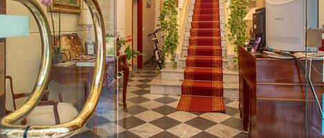 A lobby with a checkered floor, a grand staircase, a chandelier, and a Sony TV.