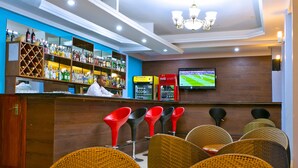 Una zona de bar con un cantinero, estantes llenos de licores, una pantalla de televisión y sillas de mimbre.