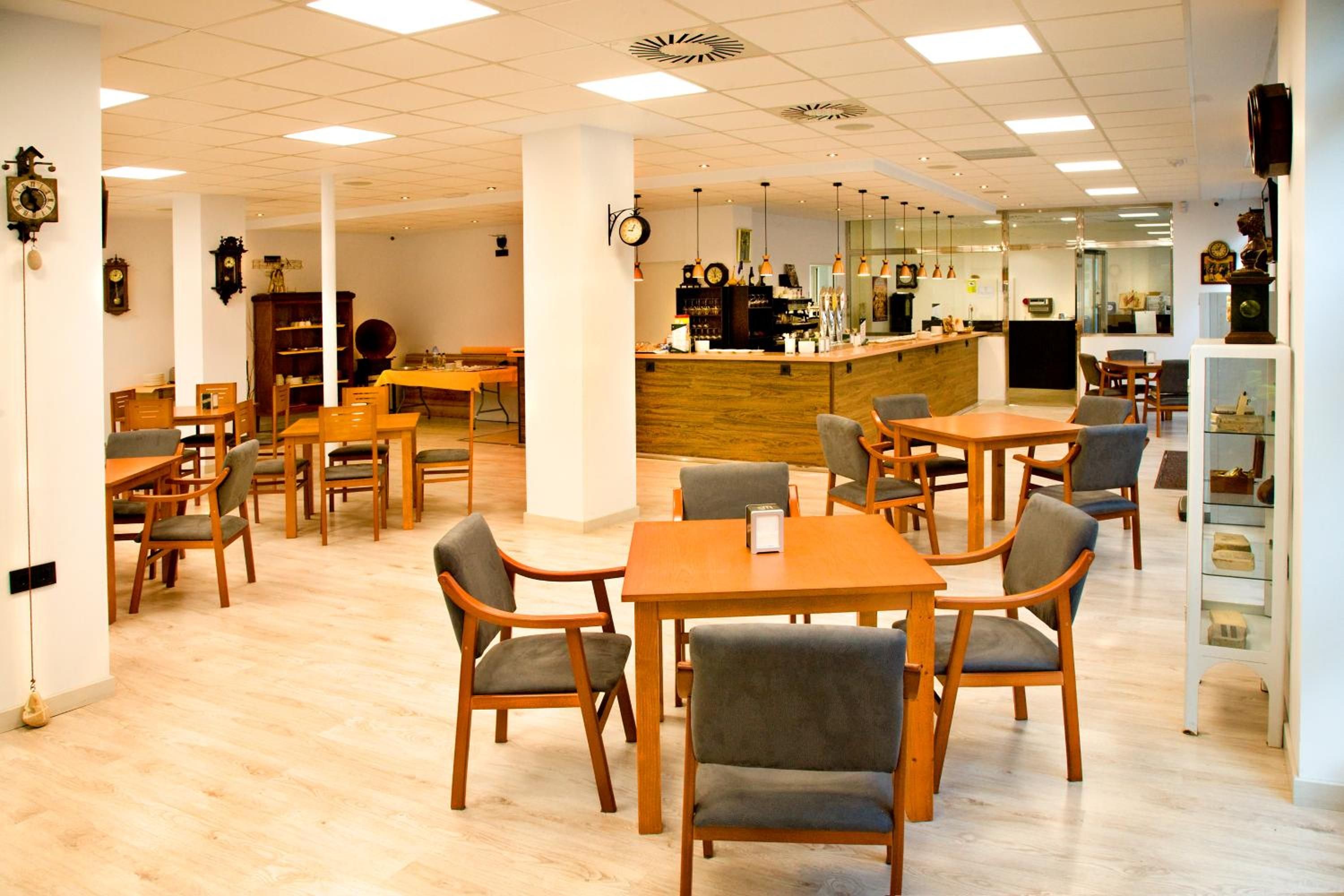 A cafe with multiple tables and chairs, a bar area, and a display of clocks on the walls.