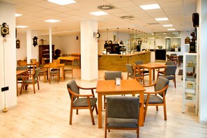 A cafe with multiple tables and chairs, a bar area, and a display of clocks on the walls. - Imprenta Musical Alojamiento (Astorga)