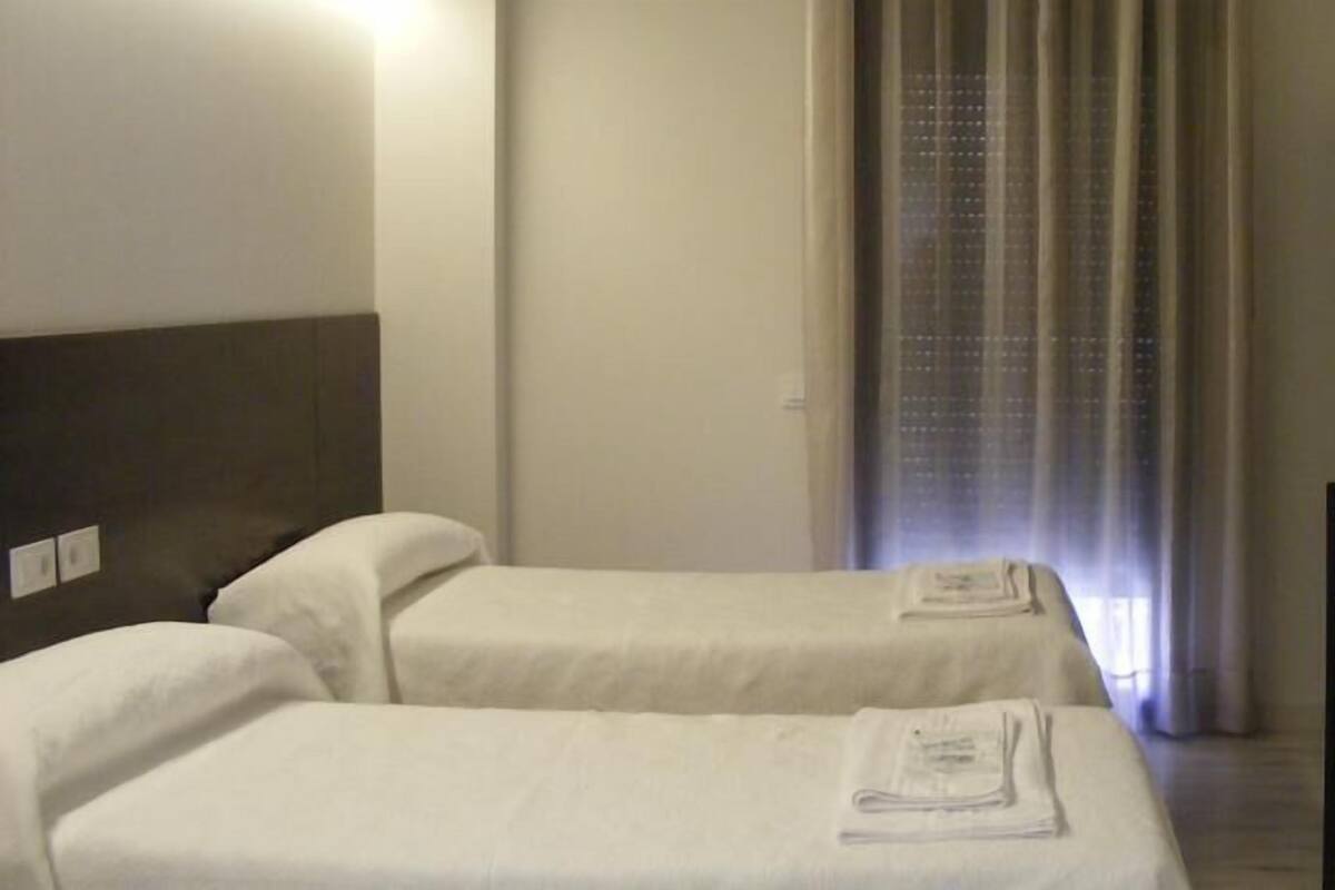 A hotel room with two single beds, a desk, a chair, and a TV.