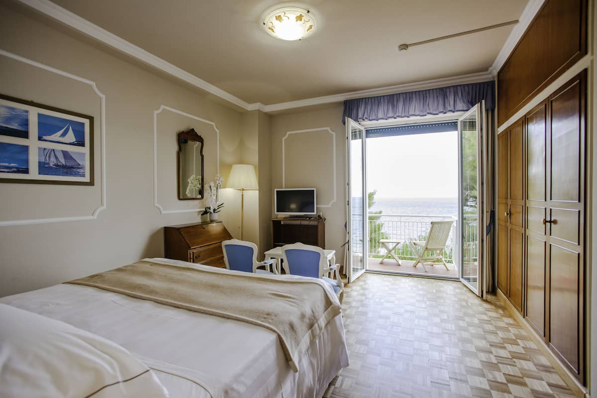 A hotel room with a bed, a desk with a chair, a television, and a balcony with a chair.