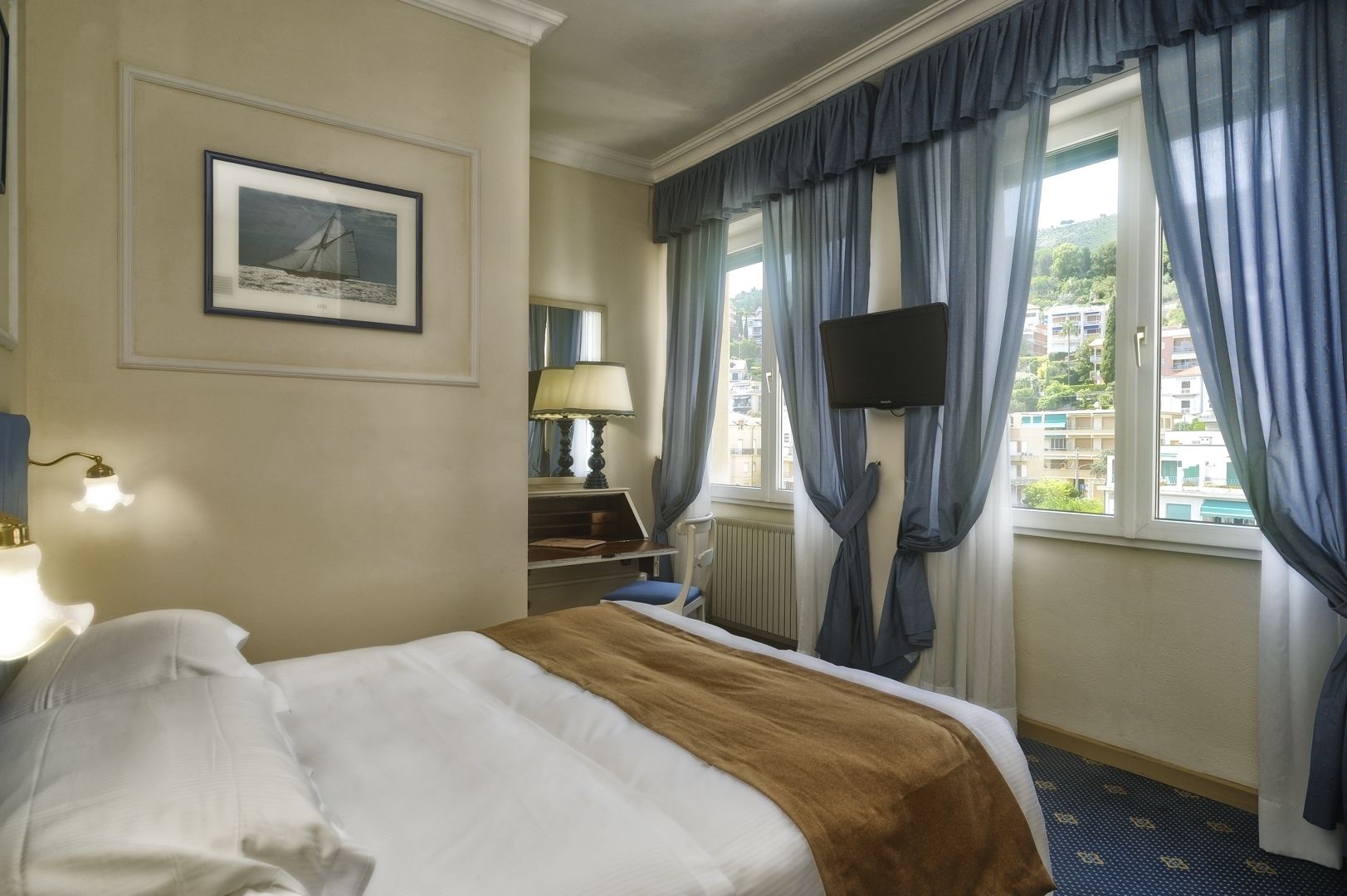Una habitación de hotel con cama, escritorio con lámpara, televisión y ventana con cortinas.