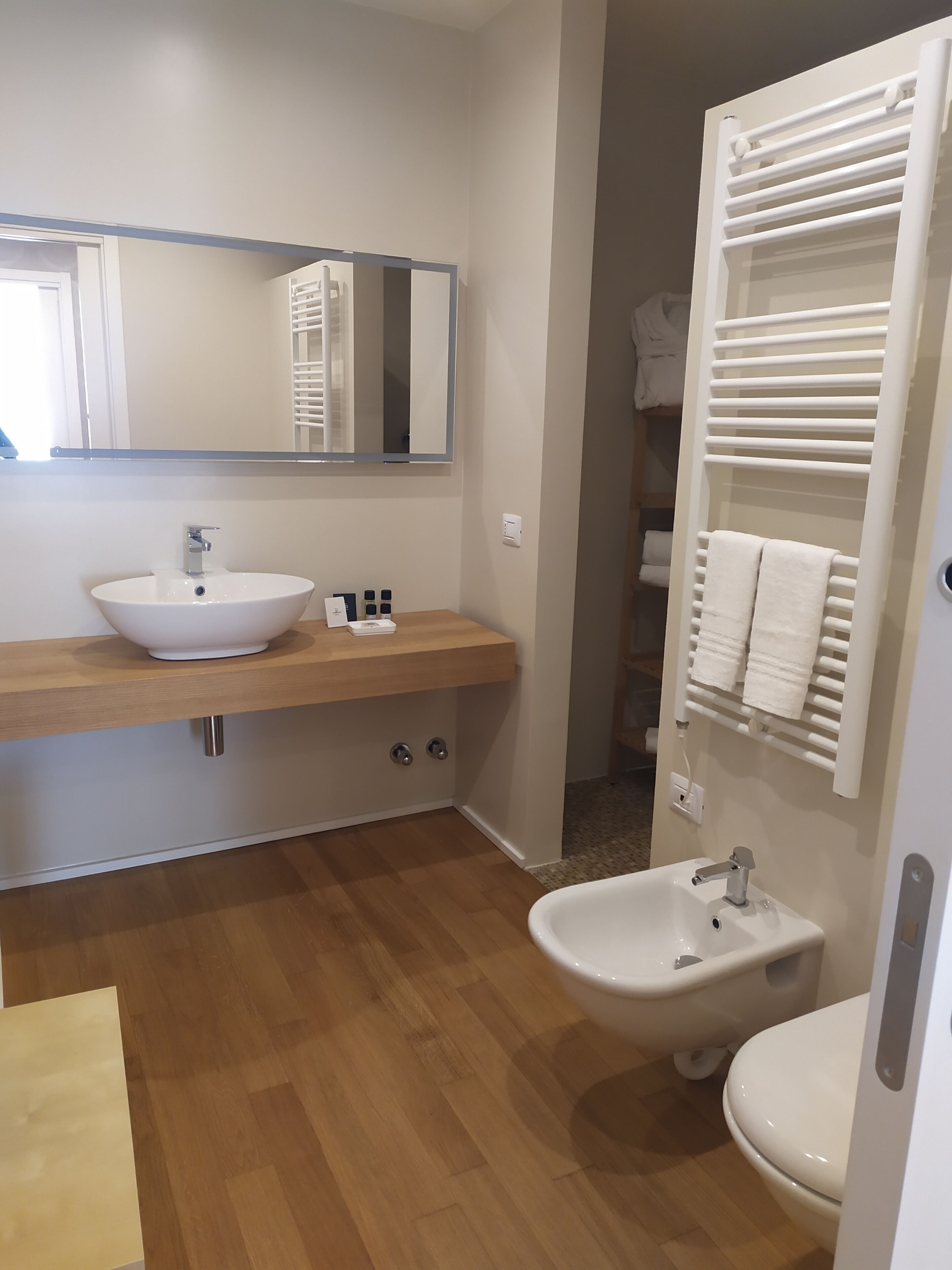 Un baño moderno con tocador de madera, un lavabo blanco, un bidé y un perchero para toallas.