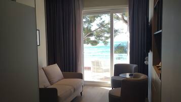 A modern living room with a sofa, a small round table, and a view of the sea through a glass door.