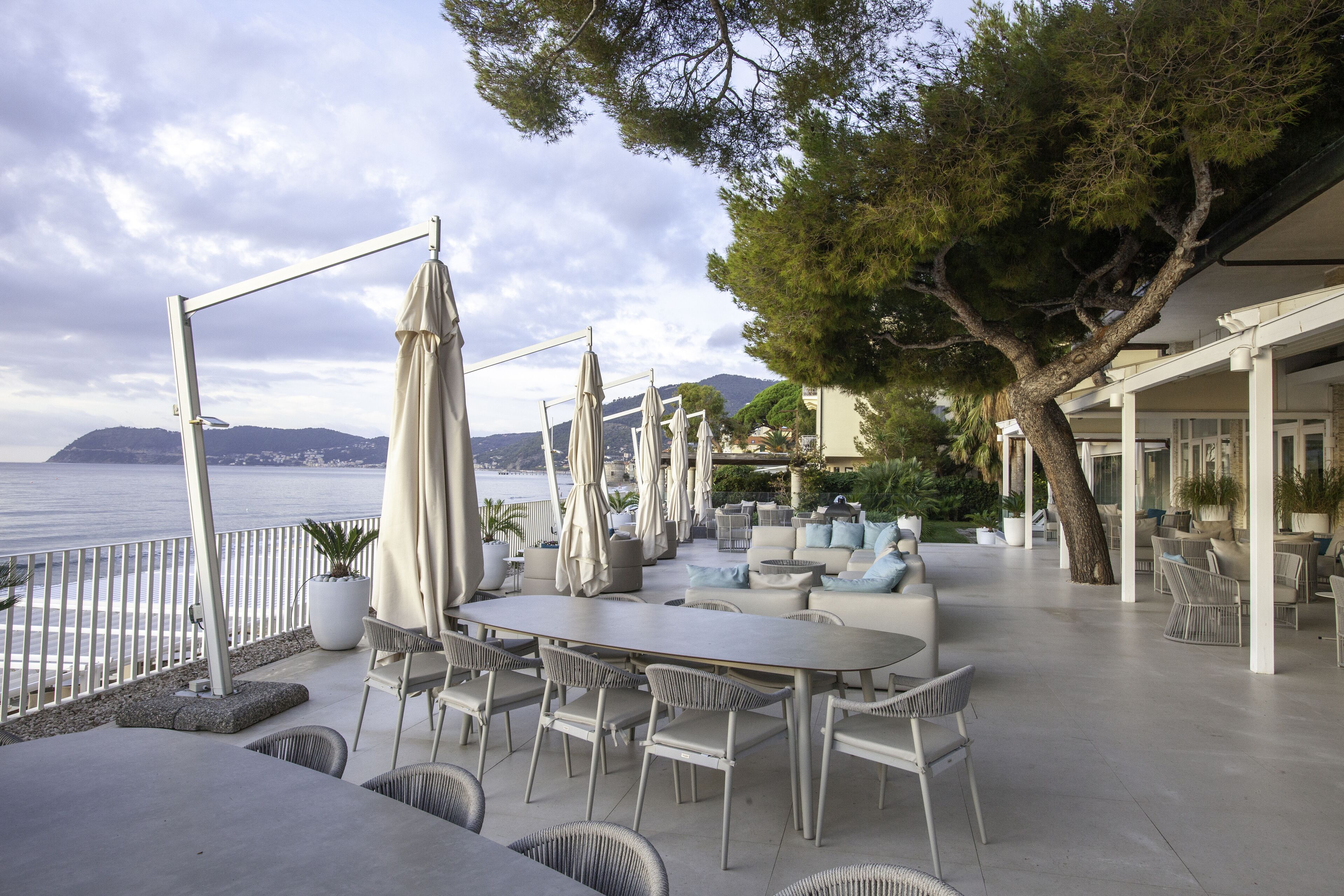 An outdoor seating area with tables and chairs, umbrellas, and potted plants.