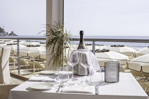 A table set for dining with a bottle of champagne, glasses, and a candle, overlooking a beach with umbrellas and lounge chairs. - Diana Grand Hotel (Alassio)