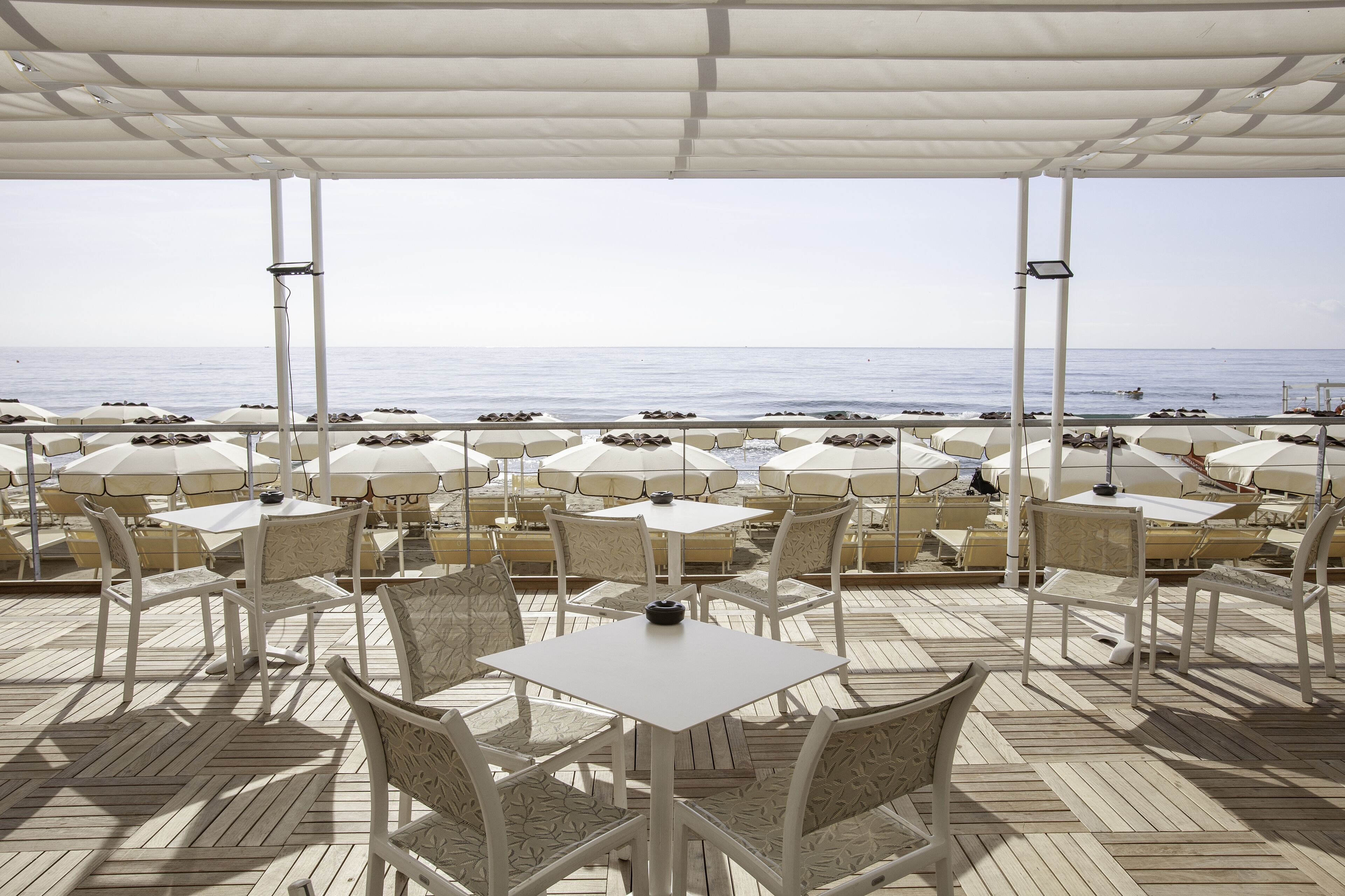 Un espacio al aire libre con mesas y sillas, sombrillas y vista al mar.