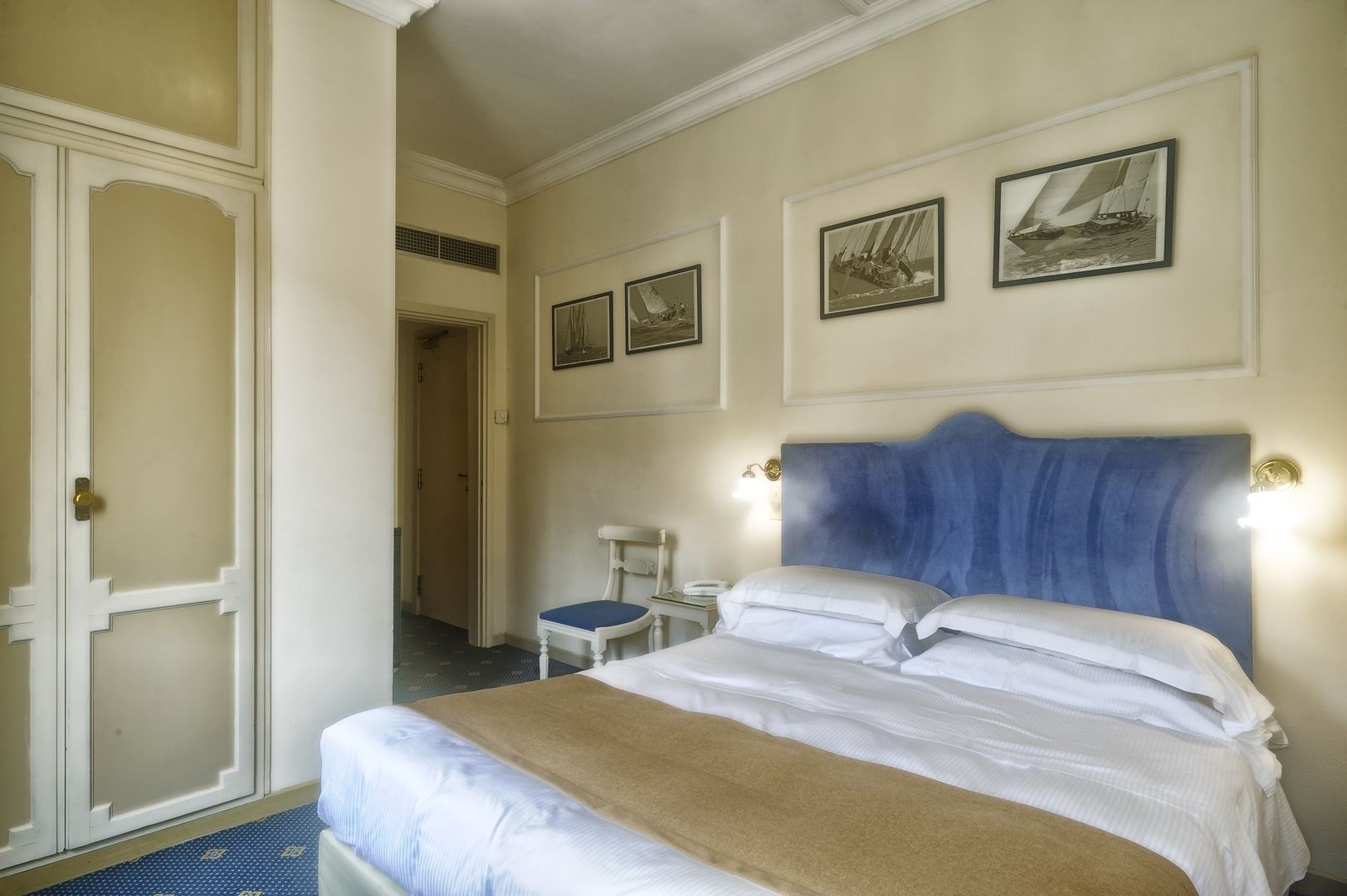 Habitación de hotel con una cama grande, una silla, un escritorio y dos cuadros en la pared.