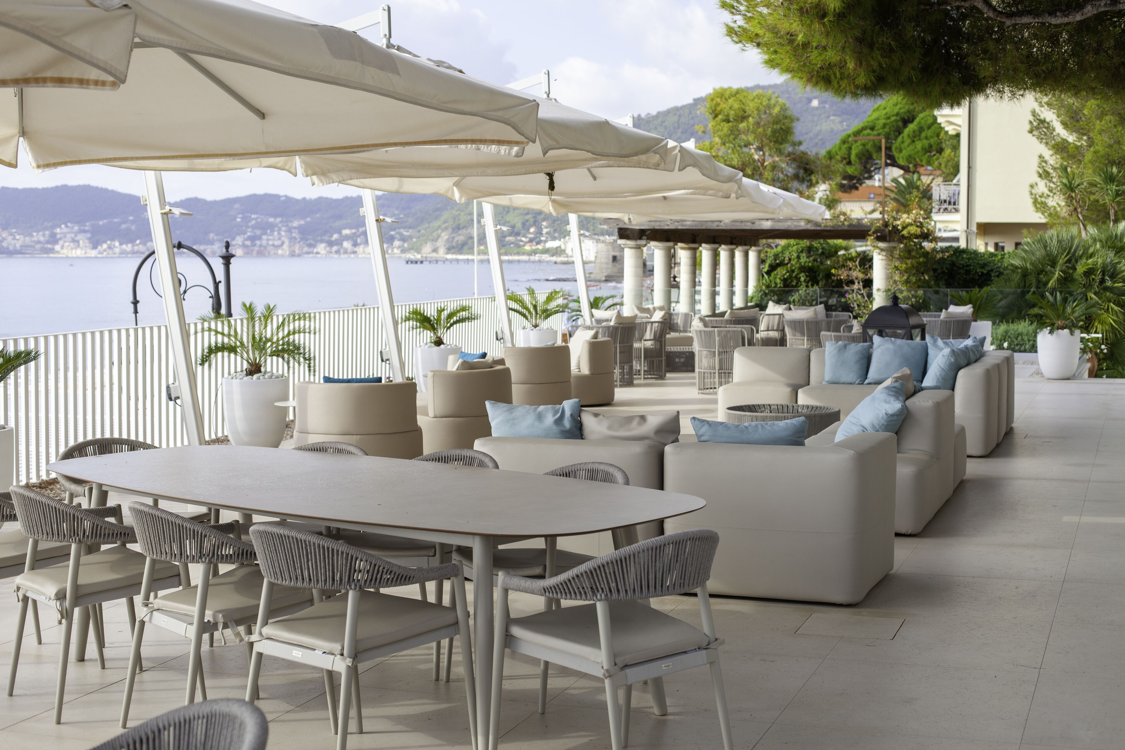 Un espace extérieur aménagé avec une table et des chaises, un canapé avec des coussins et des parasols pour faire de l’ombre.