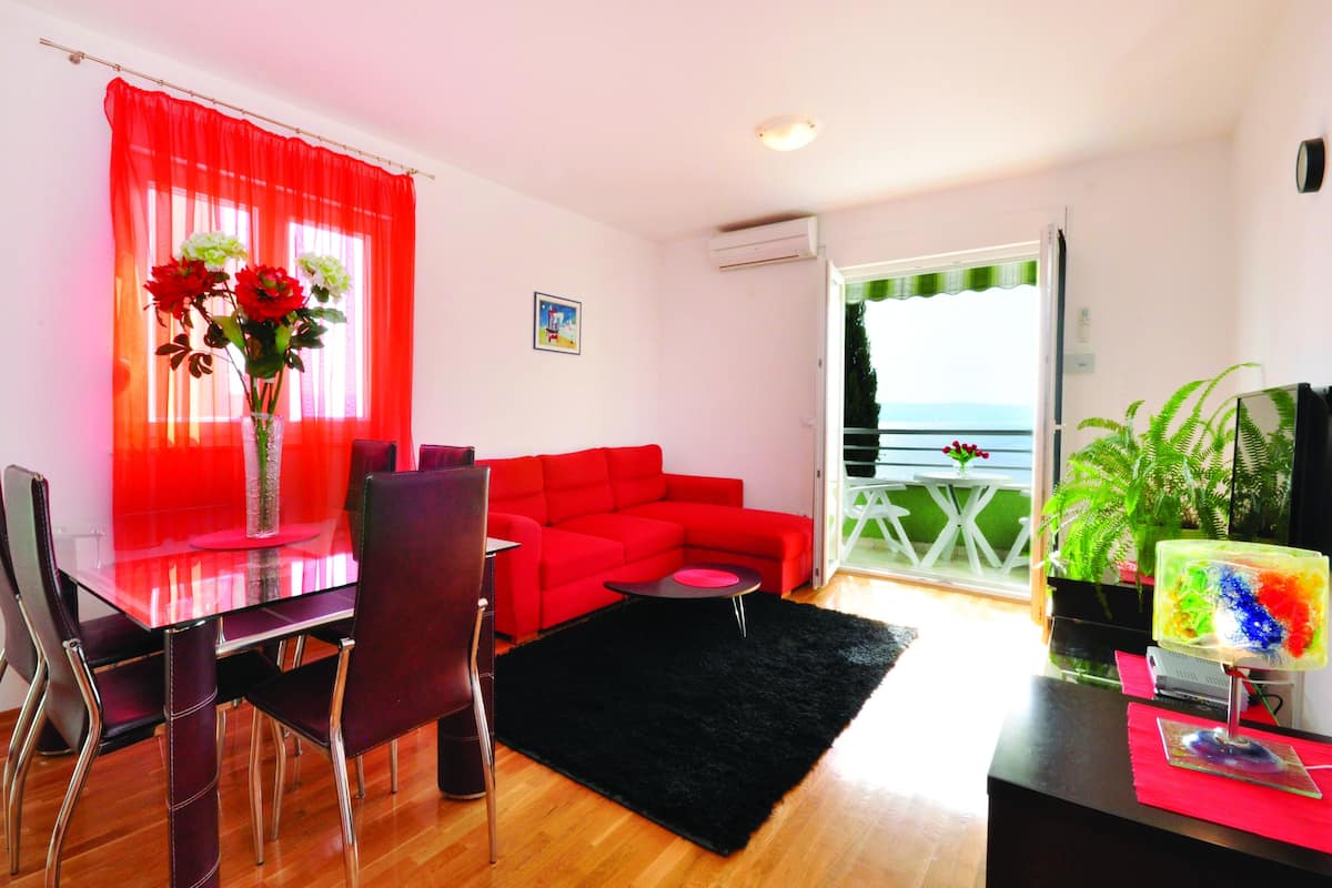A modern living room with a glass dining table, red sofa, and a black rug.