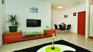 Ein modernes Wohnzimmer mit Flachbildfernseher, einem Essbereich mit Stühlen, einer roten Tür und einem Blumentopf.