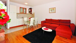 Ein modernes Wohnzimmer mit einem roten Sofa, einem Glastisch mit Stühlen und einer Küche im Hintergrund.