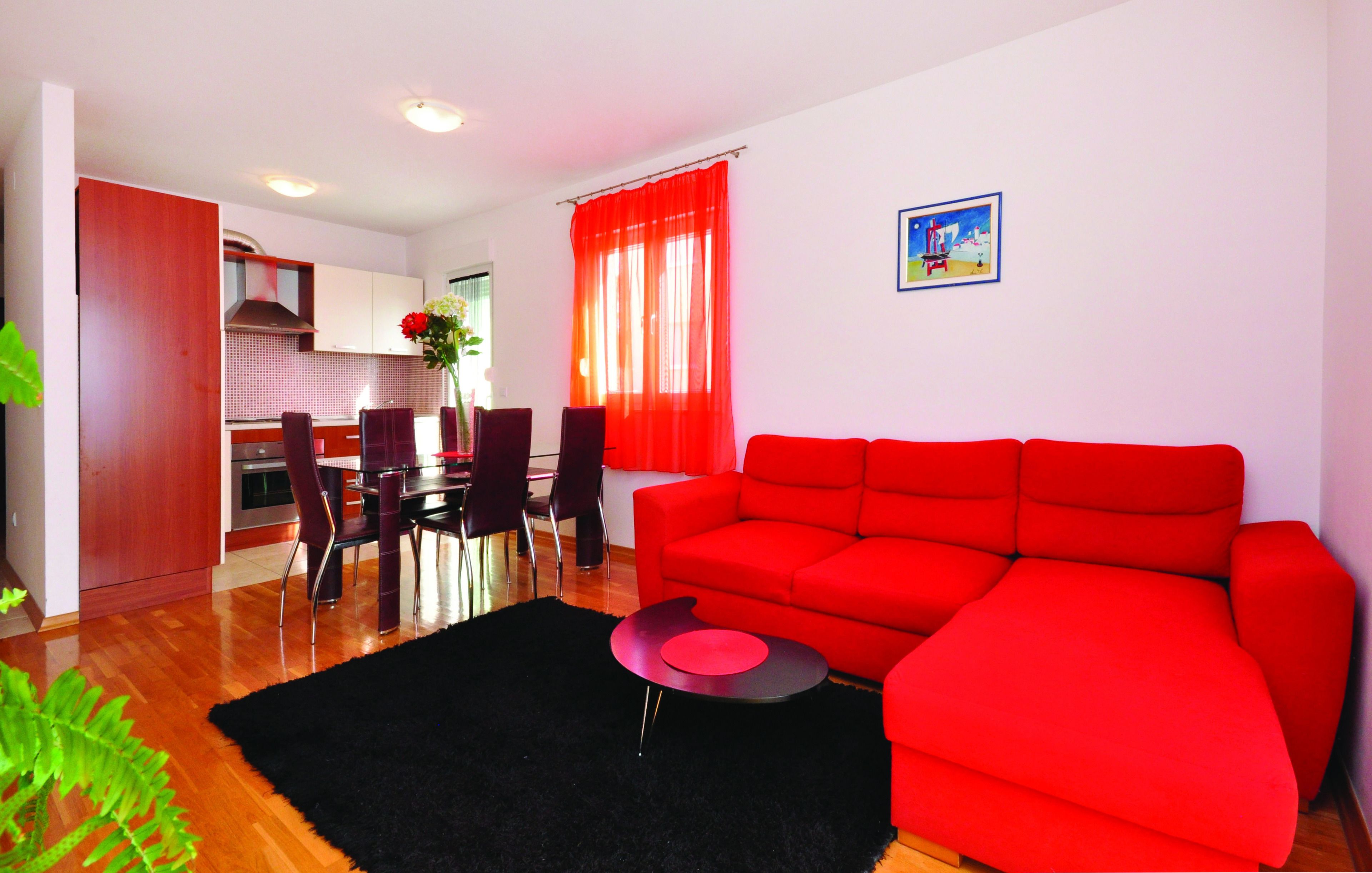 A modern living room with a red sofa, a dining table with chairs, and a kitchen in the background.