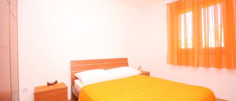 A bedroom with a bed, nightstand, and orange curtains.