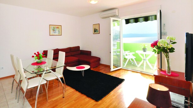 Ein Wohnzimmer mit Glastisch, rotem Sofa und Meerblick durch eine Schiebetür.