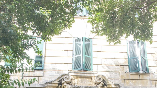 Un edifici amb una porta i persianes verdes, i una arc decoratiu.