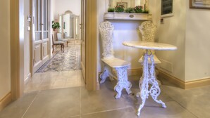 Un passadís amb mobles blancs decoratius, un paviment amb motius i un mirall sobre una estant amb plantes.